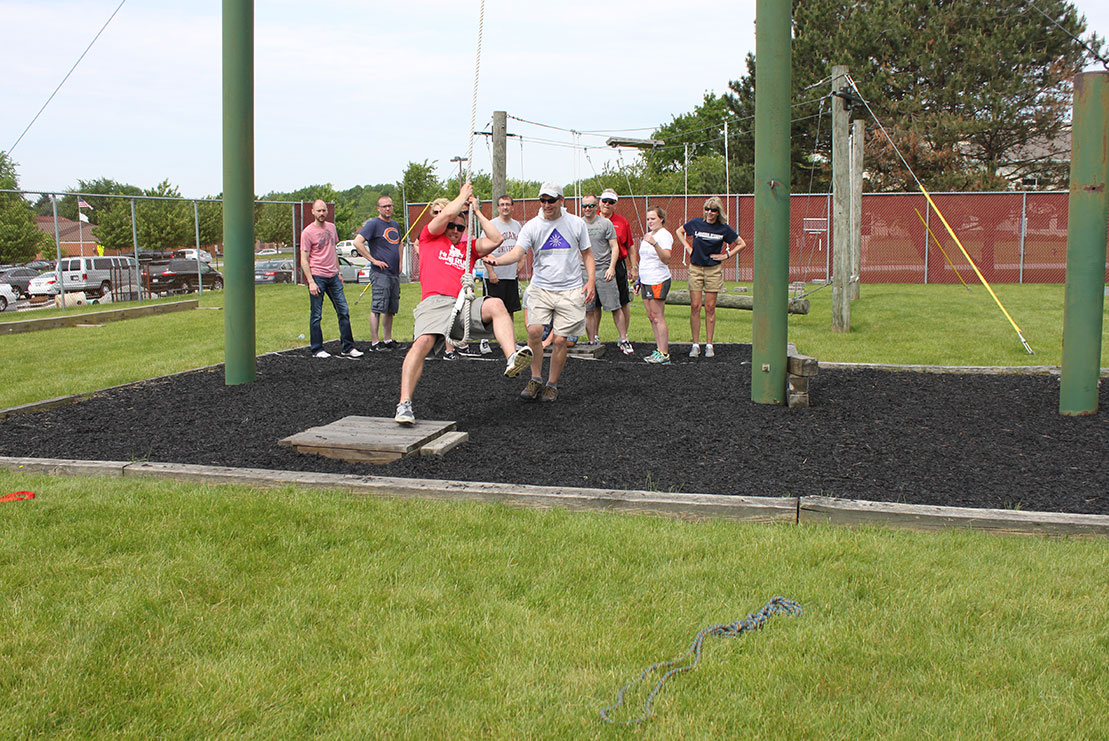 A man swings across a low ropes course challenge