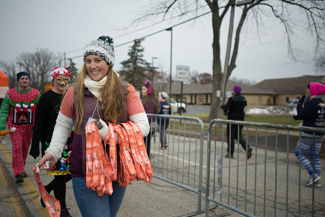 A volunteer hands out finisher medals at the 5K finish line.