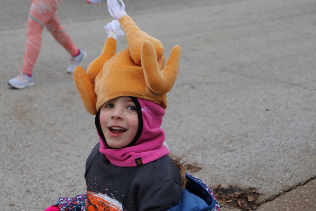 A young participant races to the finish line wearing a turkey hat.